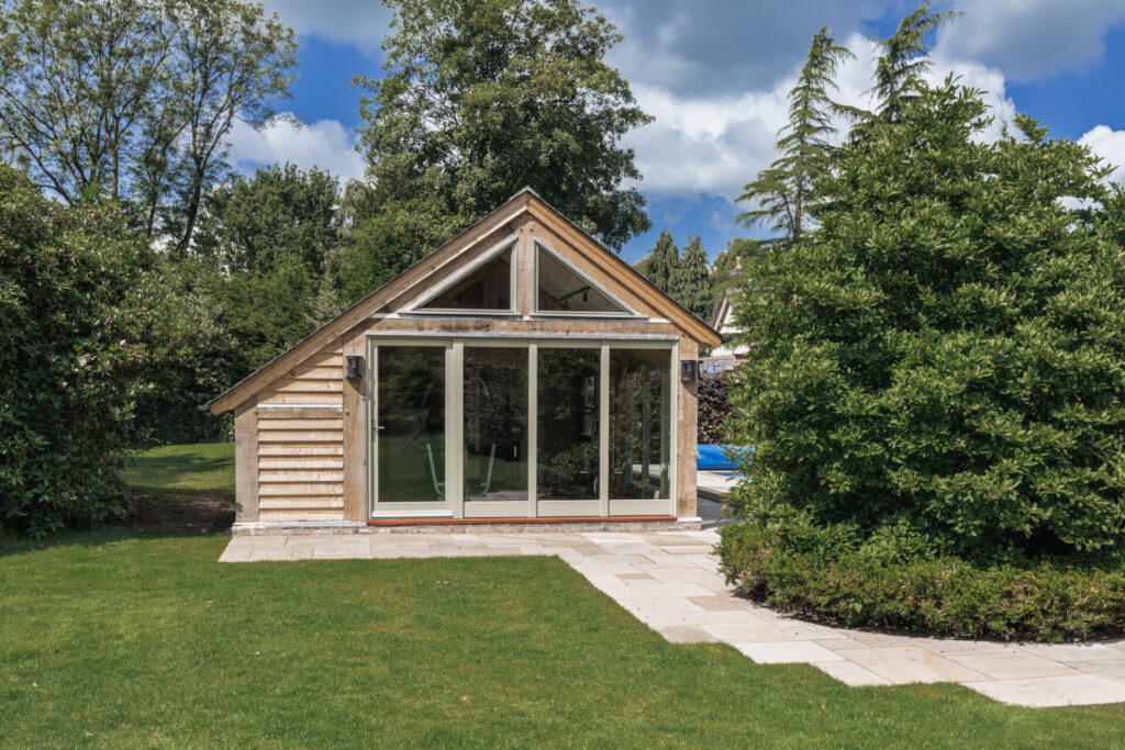 oak fram studio in garden with large glass windows next to a tree and swimming pool